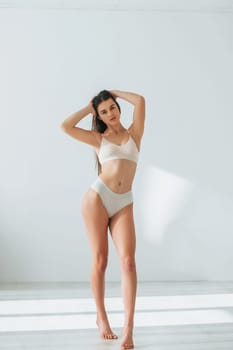 Standing in white clothes. Beautiful woman in underwear is posing indoors.