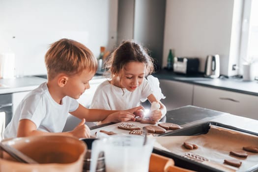 Brother and sister helping each other. Little boy and girl preparing Christmas cookies on the kitchen.