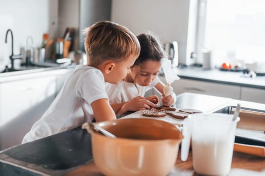 Brother and sister helping each other. Little boy and girl preparing Christmas cookies on the kitchen.