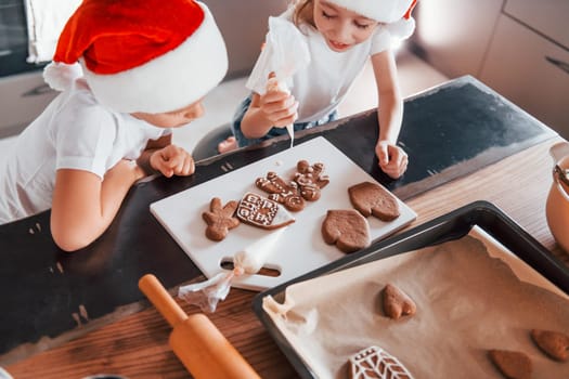 In santa hats. Little boy and girl preparing Christmas cookies on the kitchen.
