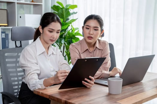 Two young office lady colleagues collaborating in modern office workspace, engaging in discussion and working together on laptop, showcasing their professionalism as modern office worker. Enthusiastic