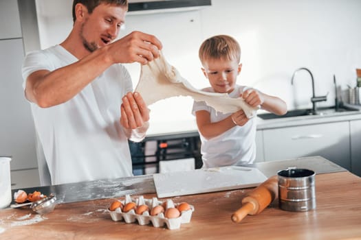 Eggs, milk and dough. Father teaching his little son with preparing of sweet christmas cookies.