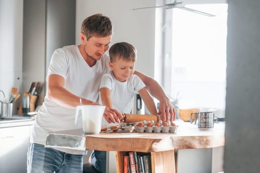 Father teaching his little son with preparing of sweet christmas cookies.