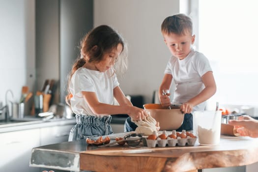 Sitting on the table. Little boy and girl preparing Christmas cookies on the kitchen.