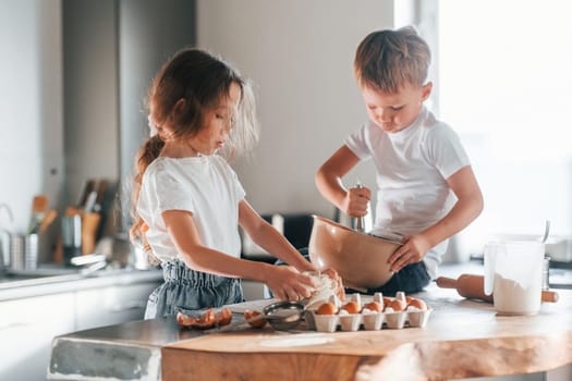 Sitting on the table. Little boy and girl preparing Christmas cookies on the kitchen.