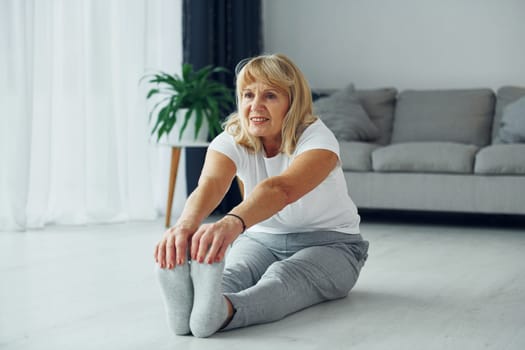 Doing fitness exercises. Senior woman with blonde hair is at home.