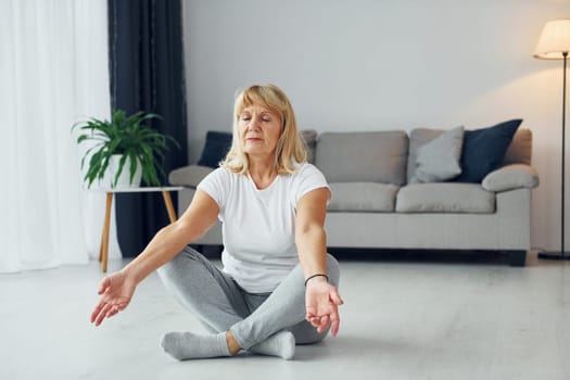 Doing fitness exercises. Senior woman with blonde hair is at home.