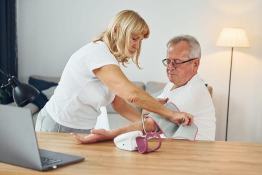 Wife measuring blood preasure of her husband. Senior man and woman is together at home.