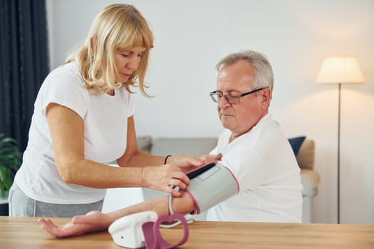 Wife measuring blood preasure of her husband. Senior man and woman is together at home.