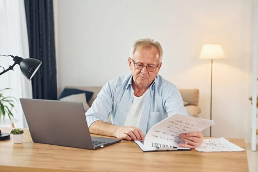 Working by using laptop. Senior man in nice clothes is at home.