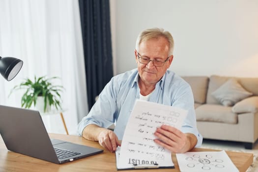 Working by using laptop. Senior man in nice clothes is at home.