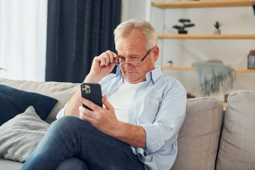 Sitting with smartphone in hands. Senior man in nice clothes is at home.