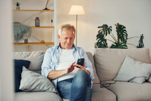 Sitting with smartphone in hands. Senior man in nice clothes is at home.