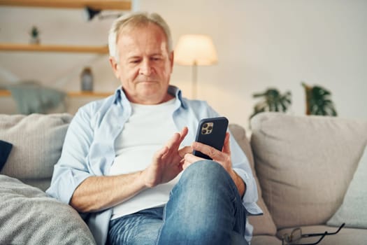 Sitting with smartphone in hands. Senior man in nice clothes is at home.