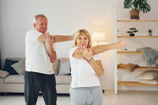 Doing stretching. Senior man and woman is together at home.