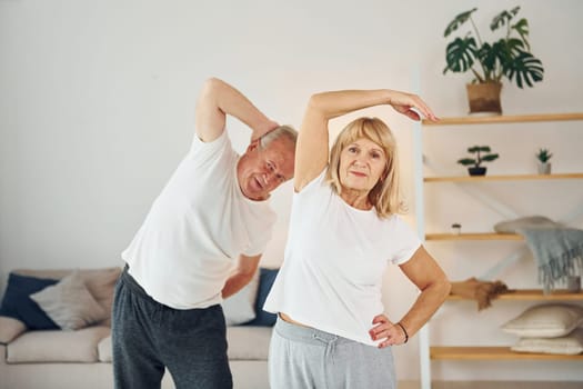 Doing stretching. Senior man and woman is together at home.