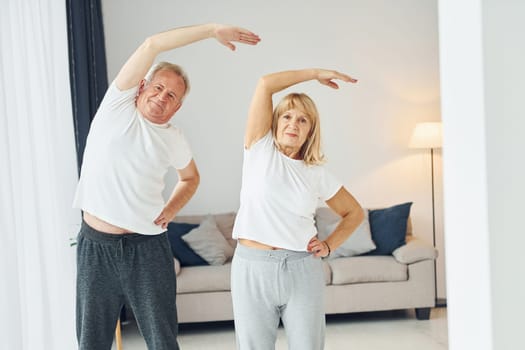 Doing stretching. Senior man and woman is together at home.