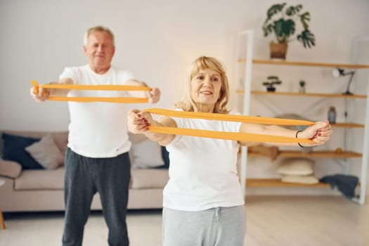 Doing stretching and fitness exercises. Senior man and woman is together at home.