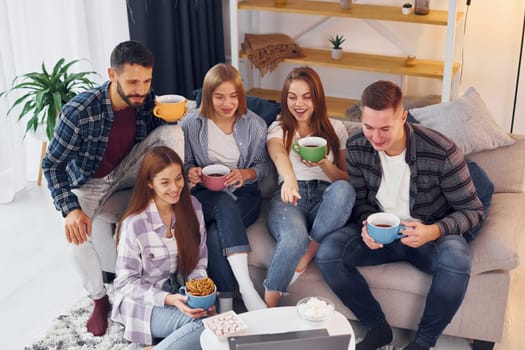With cups of drink. Group of friends have party indoors together.