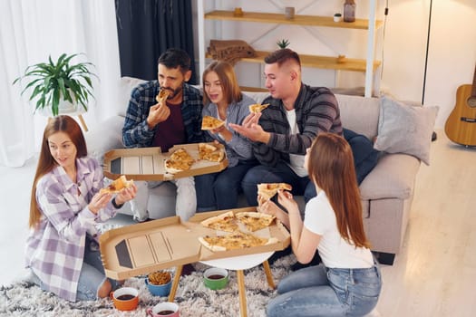 Eating delicious pizza. Group of friends have party indoors together.