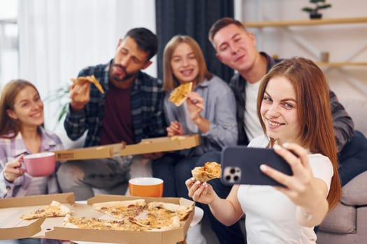 Woman making selfie. Group of friends have party indoors together.