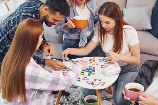 Playing puzzle game. Group of friends have party indoors together.