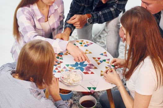 Playing puzzle game. Group of friends have party indoors together.