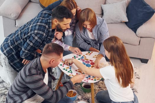 Playing puzzle game. Group of friends have party indoors together.