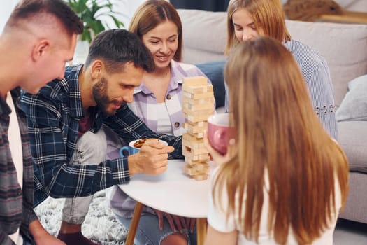 Playing wooden tower game. Group of friends have party indoors together.