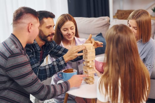 Playing wooden tower game. Group of friends have party indoors together.