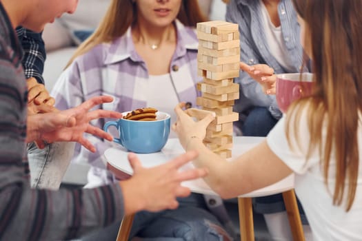 Playing wooden tower game. Group of friends have party indoors together.