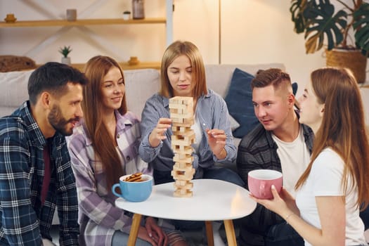 Playing wooden tower game. Group of friends have party indoors together.