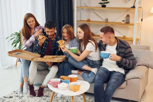 Eating food and drinking tea. Group of friends have party indoors together.