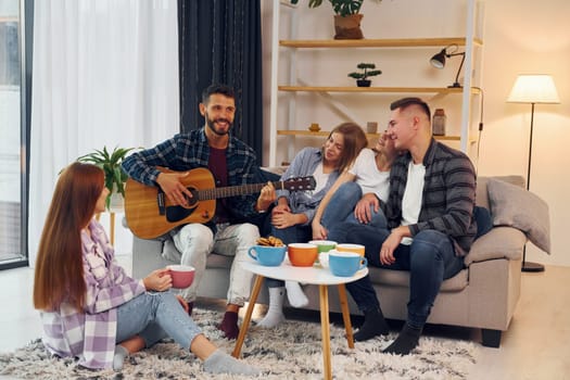 Playing acoustic guitar. Group of friends have party indoors together.