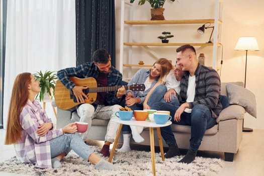 Playing acoustic guitar. Group of friends have party indoors together.