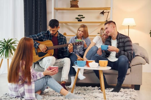 Playing acoustic guitar. Group of friends have party indoors together.