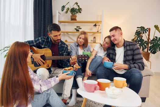 Playing acoustic guitar. Group of friends have party indoors together.