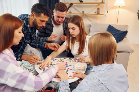 Focused at puzzle game. Group of friends have party indoors together.