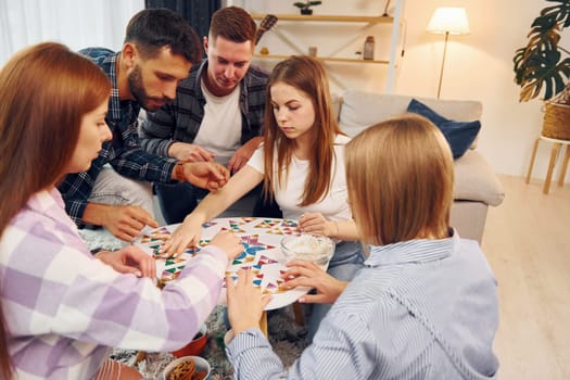 Focused at puzzle game. Group of friends have party indoors together.