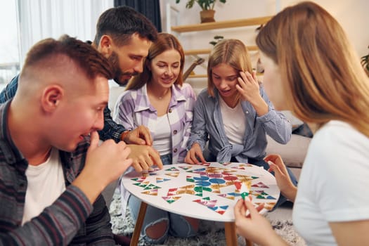 Puzzle game on the table. Group of friends have party indoors together.