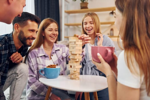 Focused on the tower building game. Group of friends have party indoors together.