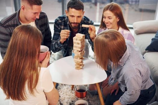 Focused on the tower building game. Group of friends have party indoors together.