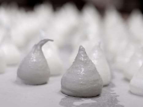 pastry chef baker artisan making white swirl and twirl meringue cones with piping bag filled with egg cream and sugar to bake for sweet preparation