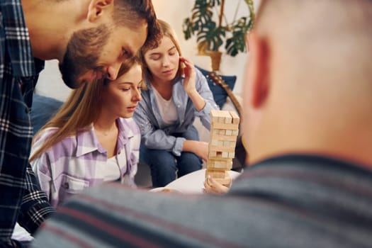 Focused on the tower building game. Group of friends have party indoors together.