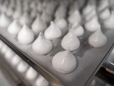pastry chef baker artisan making white swirl and twirl meringue cones with piping bag filled with egg cream and sugar to bake for sweet preparation