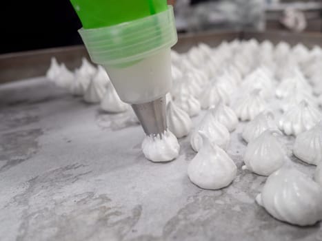 pastry chef baker artisan making white swirl and twirl meringue cones with piping bag filled with egg cream and sugar to bake for sweet preparation