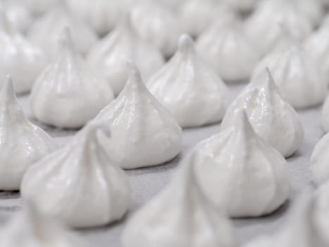 pastry chef baker artisan making white swirl and twirl meringue cones with piping bag filled with egg cream and sugar to bake for sweet preparation