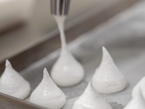 pastry chef baker artisan making white swirl and twirl meringue cones with piping bag filled with egg cream and sugar to bake for sweet preparation