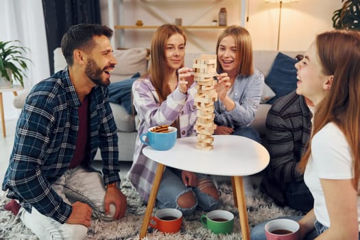 Wooden tower game on the table. Group of friends have party indoors together.