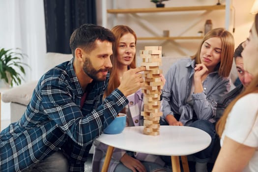 Playing wooden tower game. Group of friends have party indoors together.